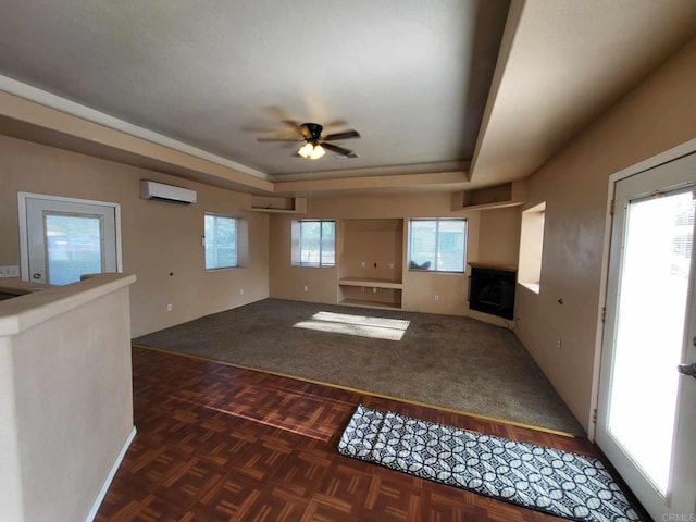 unfurnished living room with ceiling fan, a tray ceiling, and a wall mounted air conditioner