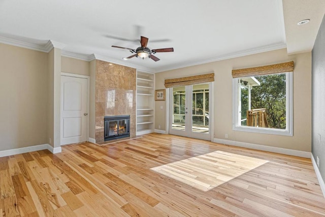 unfurnished living room featuring a tiled fireplace, built in shelves, ornamental molding, and light wood-type flooring