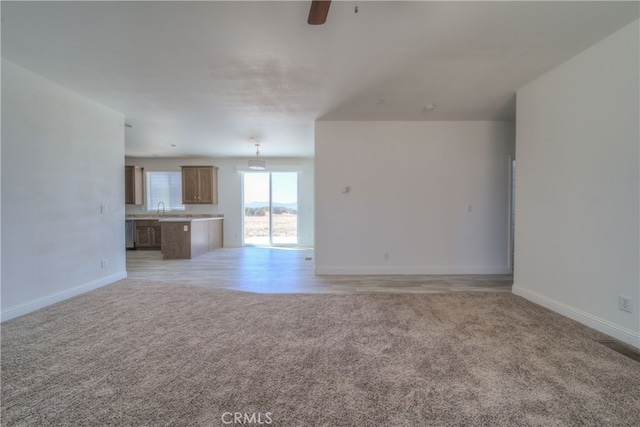 unfurnished living room with ceiling fan, light carpet, and sink