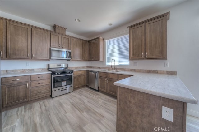 kitchen featuring appliances with stainless steel finishes, light hardwood / wood-style floors, kitchen peninsula, and sink