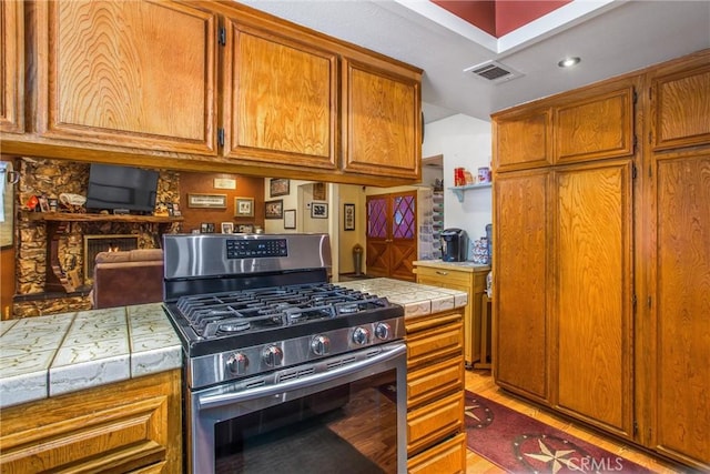 kitchen featuring stainless steel gas stove, visible vents, tile counters, and brown cabinets