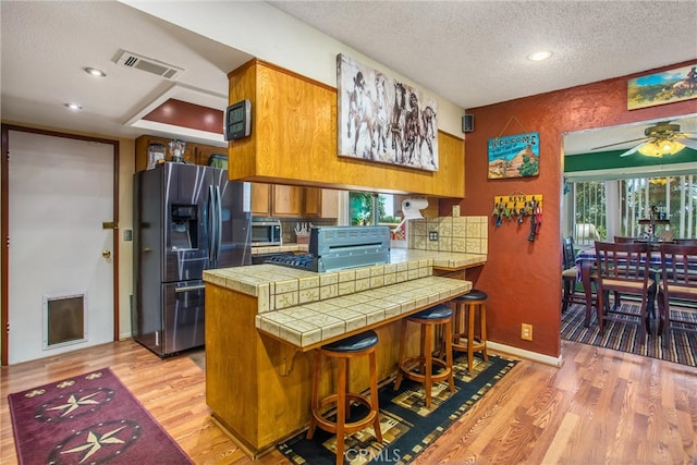 kitchen featuring light hardwood / wood-style flooring, stainless steel appliances, a textured ceiling, tile counters, and ceiling fan