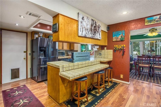 kitchen featuring visible vents, appliances with stainless steel finishes, brown cabinets, a peninsula, and light wood-style floors