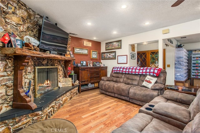 living room with light wood-type flooring, ceiling fan, a textured ceiling, and a fireplace