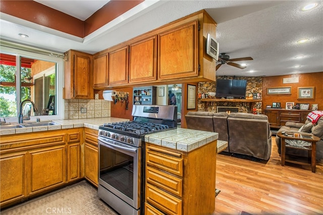 kitchen featuring sink, a fireplace, a textured ceiling, ceiling fan, and stainless steel gas range oven