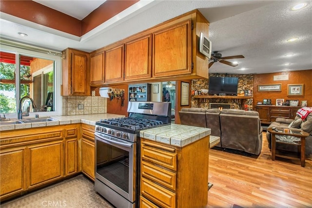 kitchen with stainless steel gas stove, brown cabinetry, open floor plan, a peninsula, and a sink