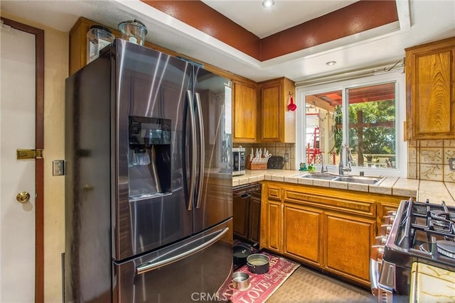 kitchen with stainless steel appliances, tile counters, decorative backsplash, brown cabinetry, and a sink