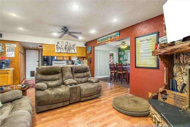 living room with ceiling fan, a textured ceiling, and light hardwood / wood-style floors