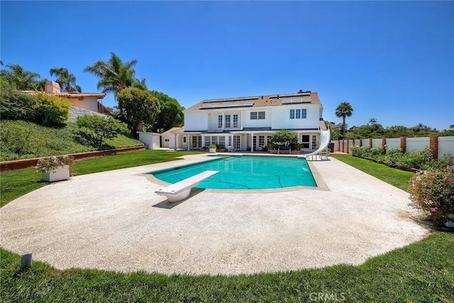 back of property with a fenced in pool, a patio, a lawn, roof mounted solar panels, and fence