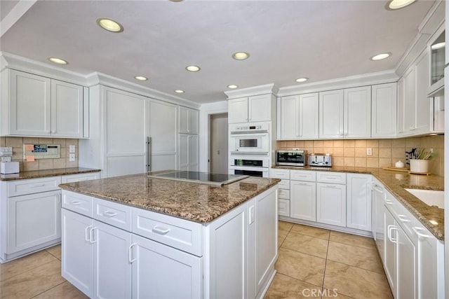 kitchen featuring white cabinets, light stone counters, a center island, black electric stovetop, and double oven