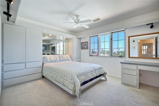 bedroom featuring visible vents, baseboards, a ceiling fan, built in study area, and light colored carpet