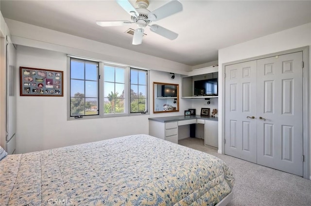 bedroom featuring a ceiling fan, built in desk, a closet, and light colored carpet