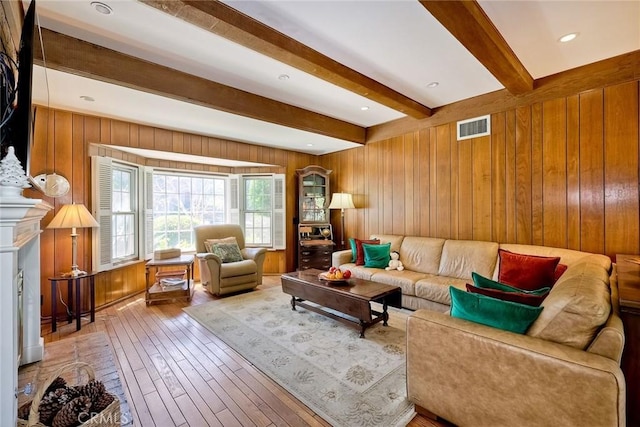 living room with beam ceiling, visible vents, wooden walls, and wood finished floors