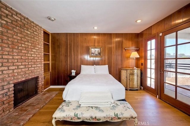 unfurnished bedroom with a brick fireplace, wooden walls, multiple windows, and wood finished floors