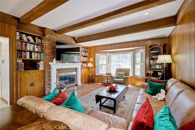 living area with beamed ceiling, wood walls, a brick fireplace, and light wood-type flooring