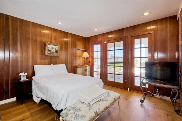 bedroom with wooden walls, recessed lighting, wood finished floors, and access to exterior