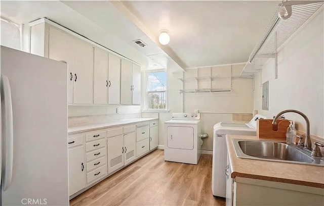 washroom featuring washing machine and dryer, cabinets, sink, electric panel, and light hardwood / wood-style flooring