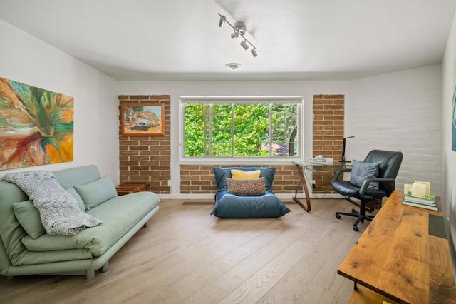 sitting room with brick wall, track lighting, and light hardwood / wood-style floors