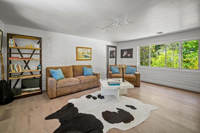 living room featuring light wood-type flooring, brick wall, and track lighting