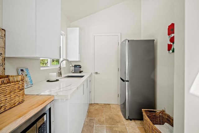 kitchen featuring white cabinets, sink, vaulted ceiling, and stainless steel refrigerator