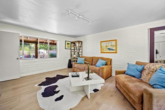 living room with brick wall, track lighting, and light hardwood / wood-style floors