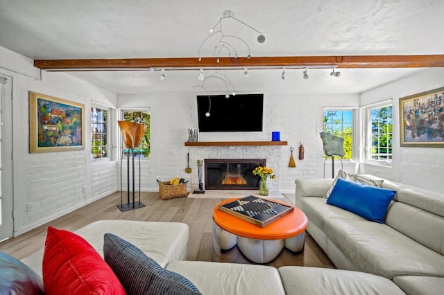 living room featuring track lighting, brick wall, beam ceiling, and light hardwood / wood-style flooring