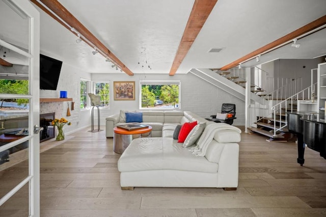 living room with rail lighting, hardwood / wood-style floors, beamed ceiling, and a stone fireplace