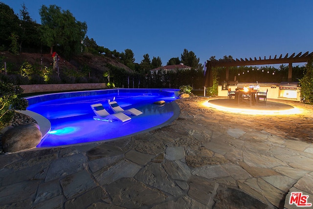 view of swimming pool featuring an outdoor kitchen, a pergola, a patio, and grilling area