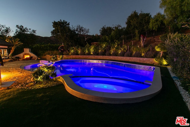 pool at dusk featuring an outdoor fireplace