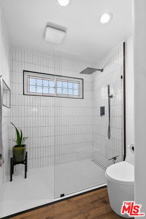 bathroom featuring tiled shower, hardwood / wood-style floors, and toilet