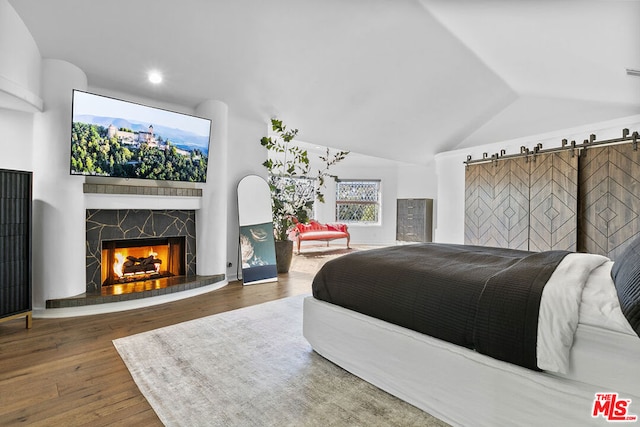 bedroom featuring a barn door, dark wood-type flooring, and lofted ceiling