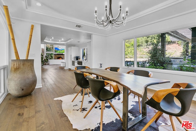 dining room with a chandelier, a tray ceiling, hardwood / wood-style flooring, a fireplace, and ornamental molding