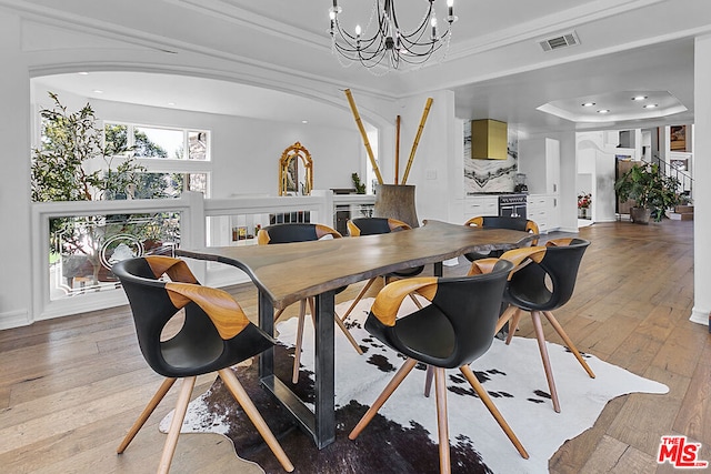 dining space with a raised ceiling, an inviting chandelier, ornamental molding, and hardwood / wood-style flooring