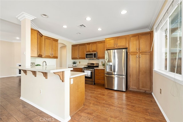 kitchen featuring appliances with stainless steel finishes, decorative columns, light hardwood / wood-style floors, and a breakfast bar