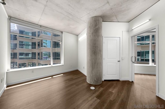 spare room with decorative columns and dark wood-type flooring