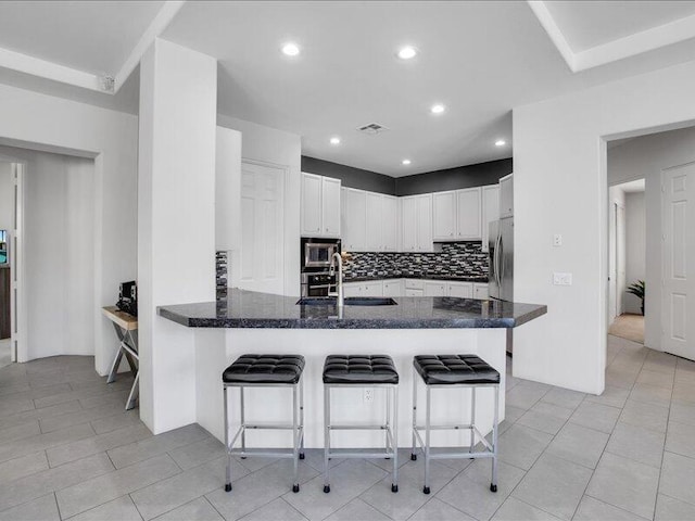 kitchen featuring kitchen peninsula, a kitchen breakfast bar, tasteful backsplash, stainless steel appliances, and white cabinets