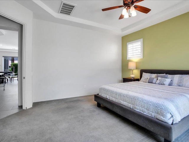 carpeted bedroom featuring ceiling fan and a raised ceiling