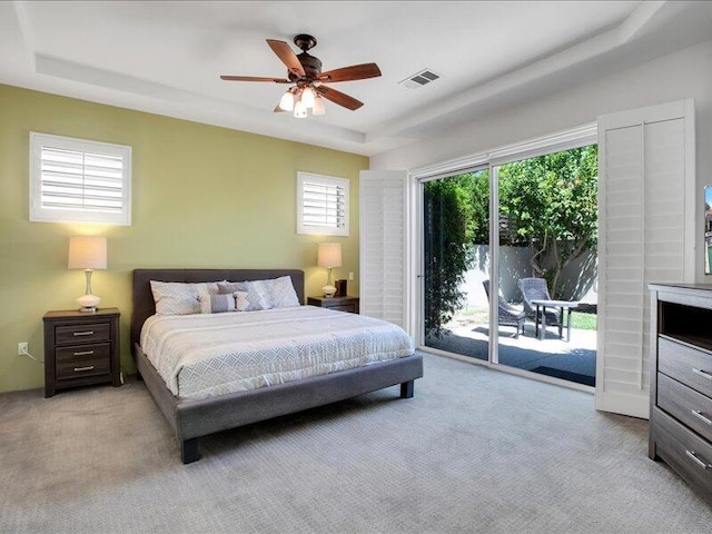 carpeted bedroom featuring access to outside, ceiling fan, and a tray ceiling