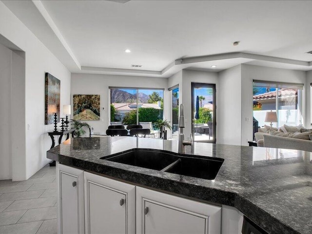 kitchen with white cabinets, a wealth of natural light, dark stone counters, and sink