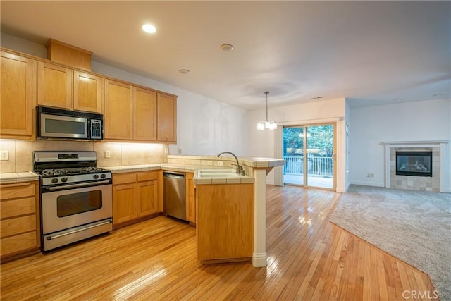 kitchen with sink, hanging light fixtures, light hardwood / wood-style flooring, kitchen peninsula, and stainless steel appliances