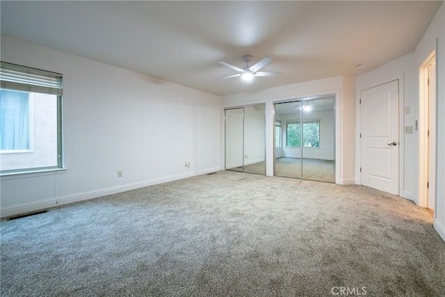 unfurnished bedroom with ceiling fan, two closets, carpet floors, and multiple windows