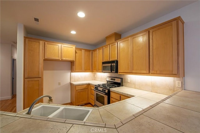 kitchen with appliances with stainless steel finishes, light brown cabinets, tile countertops, and sink