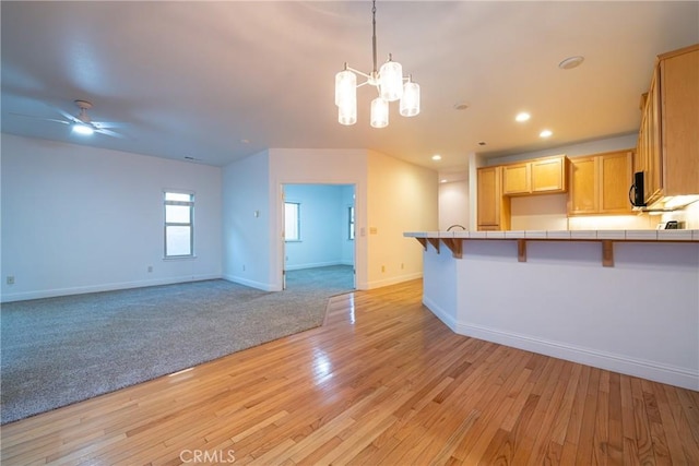 kitchen featuring a breakfast bar area, tile countertops, light brown cabinets, and light wood-type flooring