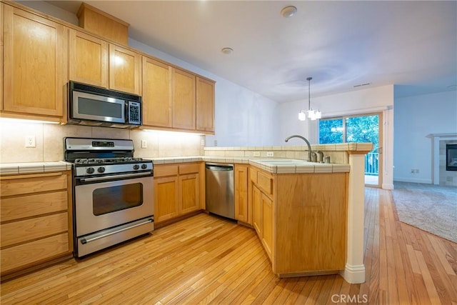 kitchen featuring kitchen peninsula, stainless steel appliances, sink, light hardwood / wood-style flooring, and tile counters