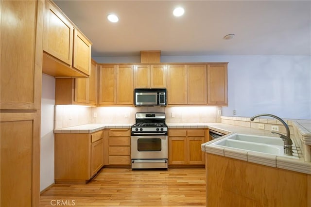 kitchen with tile countertops, light wood-type flooring, sink, and appliances with stainless steel finishes