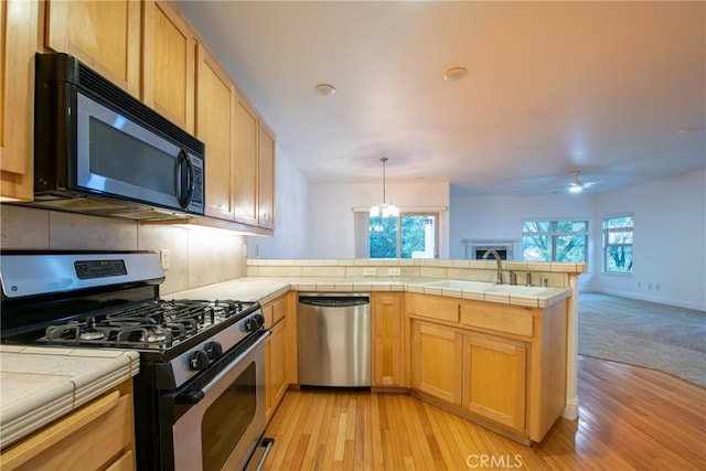 kitchen with pendant lighting, sink, light hardwood / wood-style floors, kitchen peninsula, and stainless steel appliances