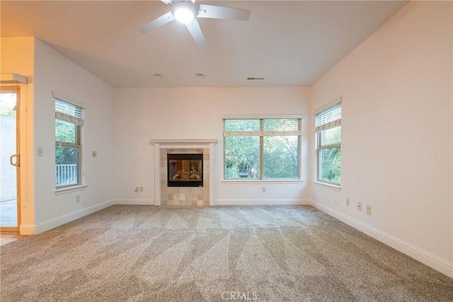 unfurnished living room with ceiling fan, light colored carpet, a fireplace, and a wealth of natural light