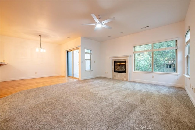 unfurnished living room featuring a tiled fireplace, light hardwood / wood-style flooring, and ceiling fan with notable chandelier