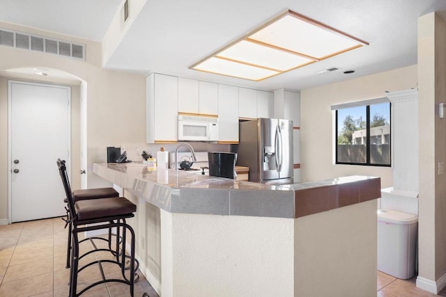 kitchen with kitchen peninsula, stainless steel refrigerator with ice dispenser, white cabinets, a breakfast bar area, and light tile patterned flooring