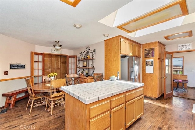 kitchen featuring stainless steel fridge with ice dispenser, tile countertops, wood-type flooring, french doors, and a center island